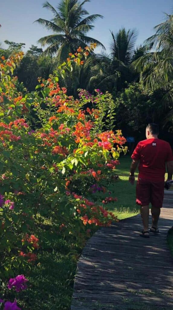 Guest walking the flower-lined wooden boardwalk through the grounds at Les Cayalines Résidence Hôtelière