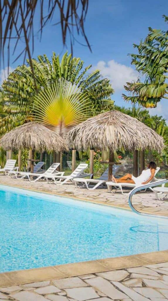 Guests relaxing by the pool at Les Cayalines Résidence Hôtelière under thatched palm umbrellas