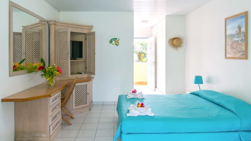Clean simple guest room at Les Cayalines Résidence Hôtelière with turquoise linens and Caribbean-style furnishings