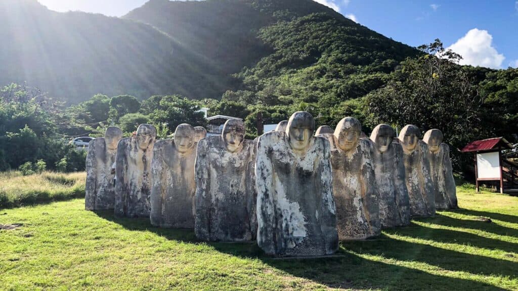 Ancient stone sculpture figures standing in a green field backed by mountains in Martinique island