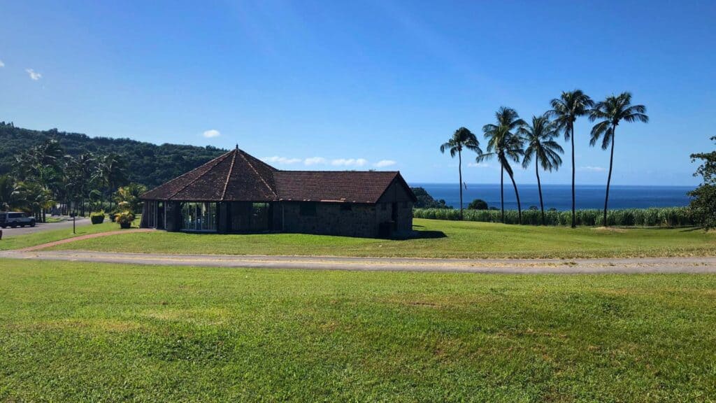 Dark timber pavilion surrounded by palm trees and green fields near the Martinique France coast
