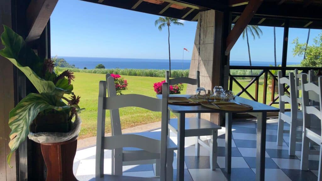Open air dining table set with a view of lush green fields and the Caribbean Sea in Martinique island