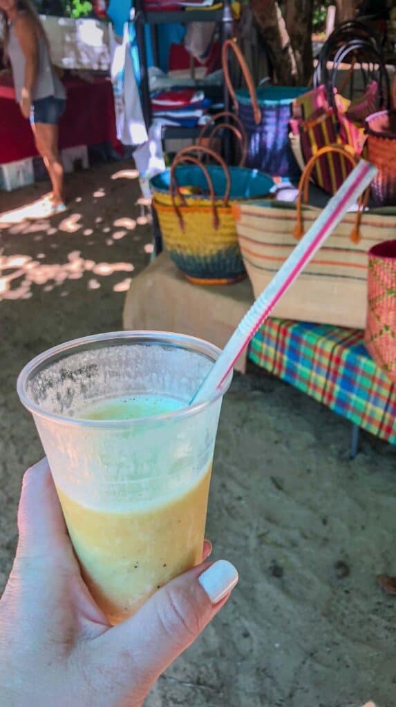 Fresh fruit smoothie held up at a Martinique travel guide outdoor market with woven baskets behind