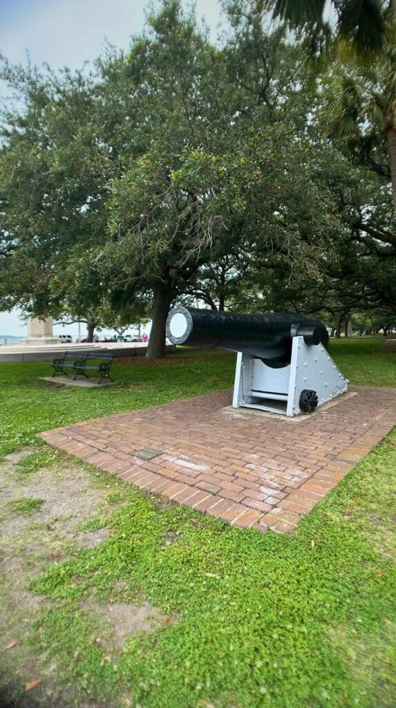 Civil War cannon on a brick platform under oak trees at White Point Garden, a relaxing date night in Charleston spot
