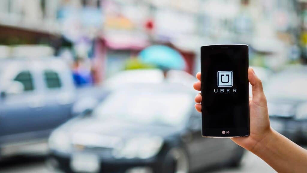 Smartphone showing the Uber app held over a blurred city street, illustrating how to book a rideshare to the cruise port.