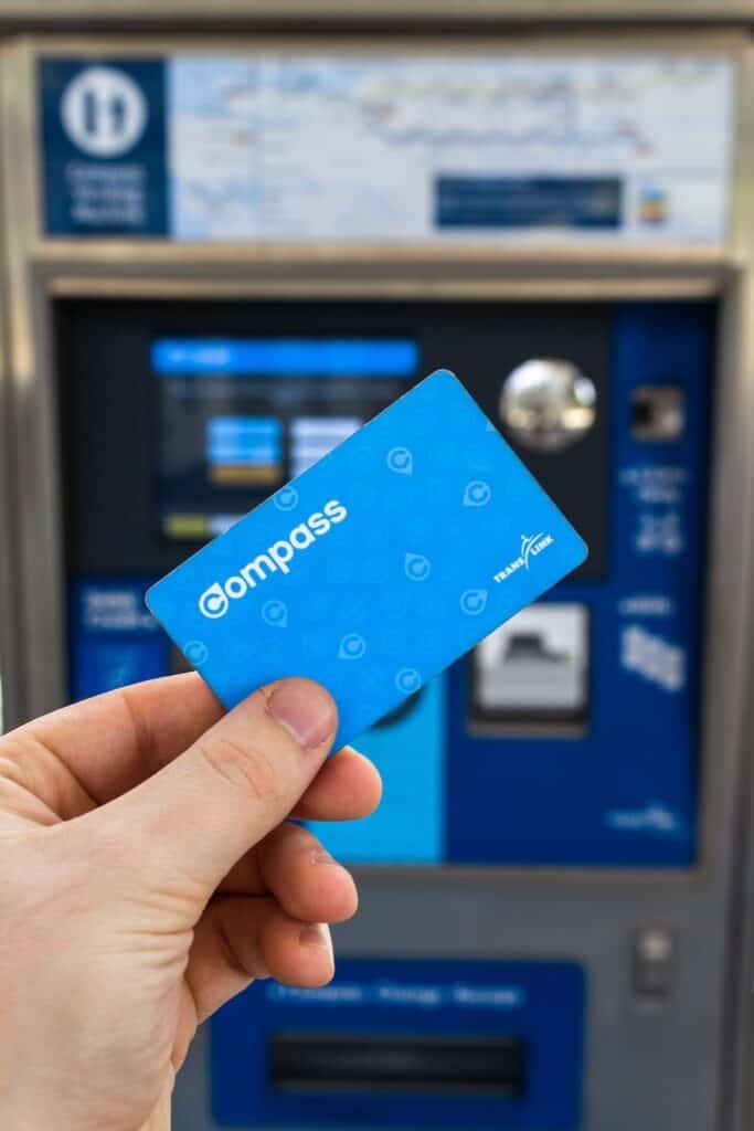 Hand holding a blue Compass Card in front of a transit ticket machine, used to pay for SkyTrain rides to the cruise port.
