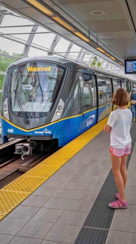 Child standing on a SkyTrain platform next to a train labeled "Waterfront," the final stop near the Vancouver cruise port.