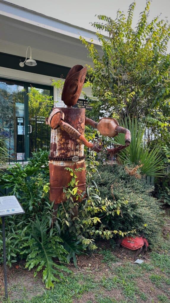 Rusted metal sculpture of a musician playing a guitar surrounded by greenery outside a building in Ocean Springs Mississippi.