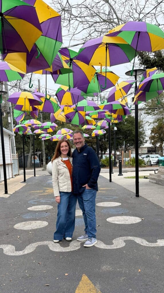 Couple standing under a canopy of colorful hanging umbrellas on a downtown Ocean Springs street, a popular photo spot and one of the fun things to do in Ocean Springs.