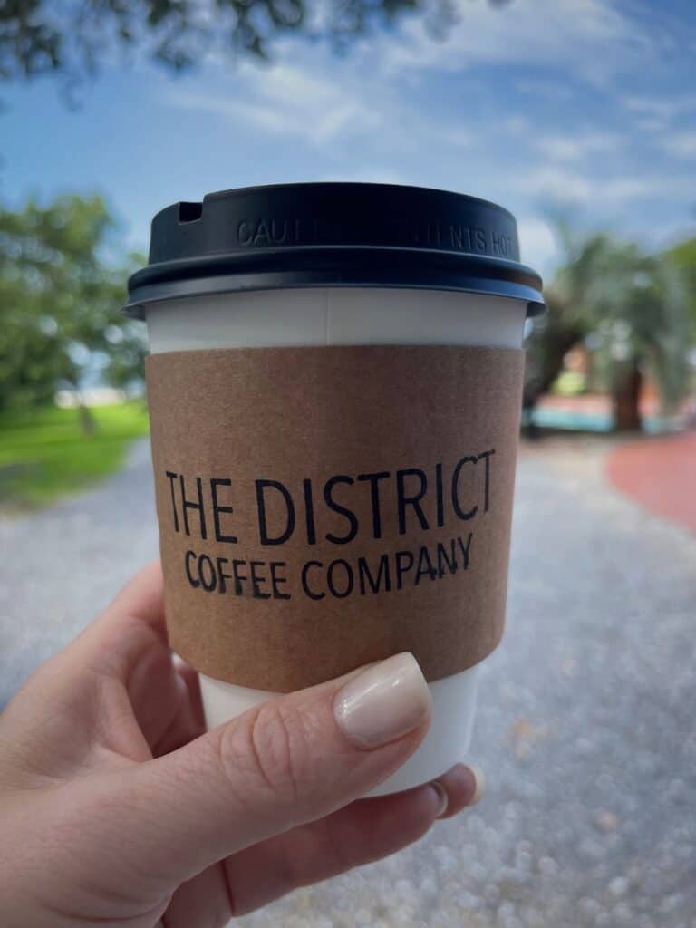 A hand holds a District Coffee Company cup, one of the go-to places to eat in Ocean Springs, MS for breakfast.