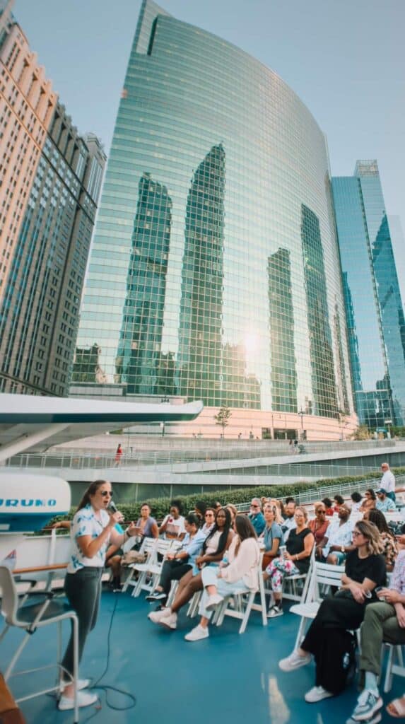 Guide narrating to passengers beside curved glass towers on a chicago architecture river cruise