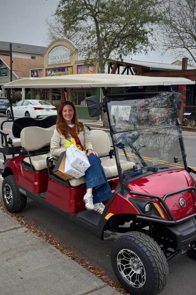 Woman sitting in a red golf cart parked along a street in downtown Ocean Springs, showing a popular way to get around while exploring shops and restaurants.