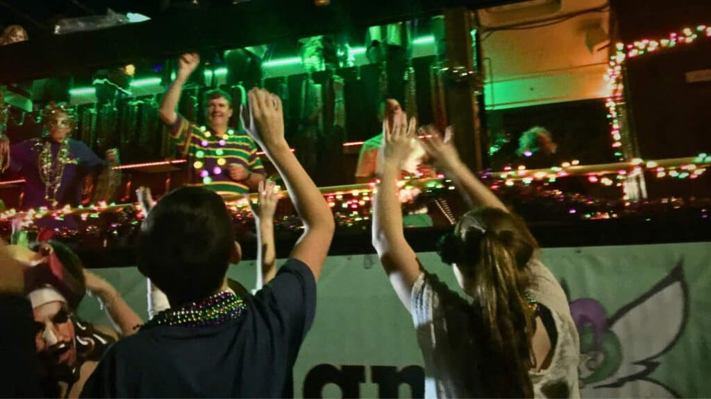 Mardi Gras parade in Ocean Springs with colorful floats and people reaching for beads along the street.
