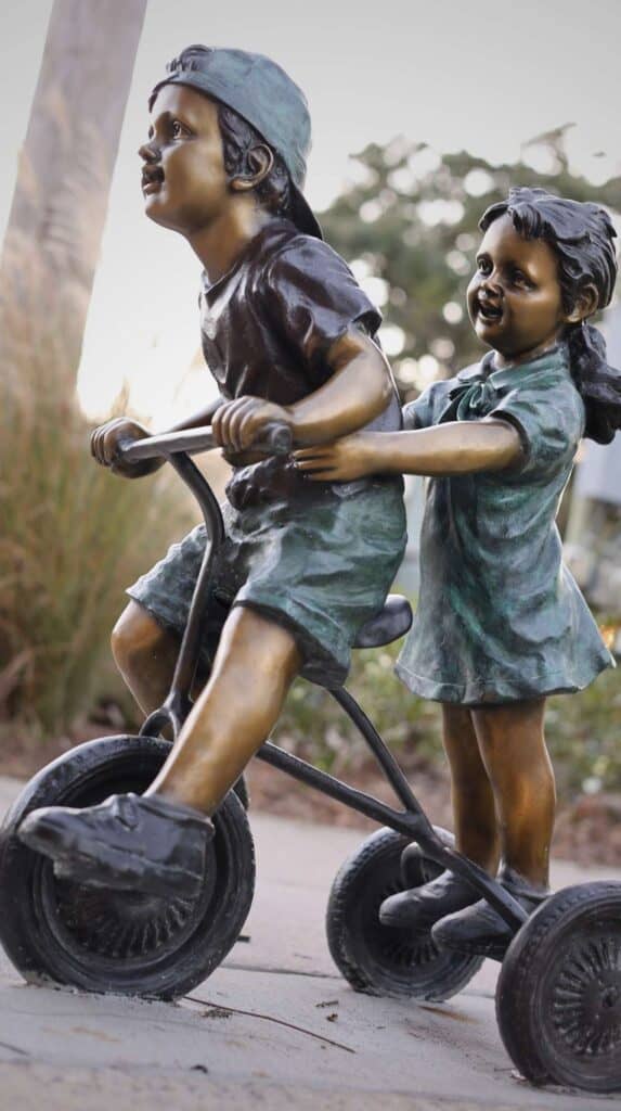 Bronze sculpture of two children riding a bicycle together, part of the public art scene in downtown Ocean Springs Mississippi.