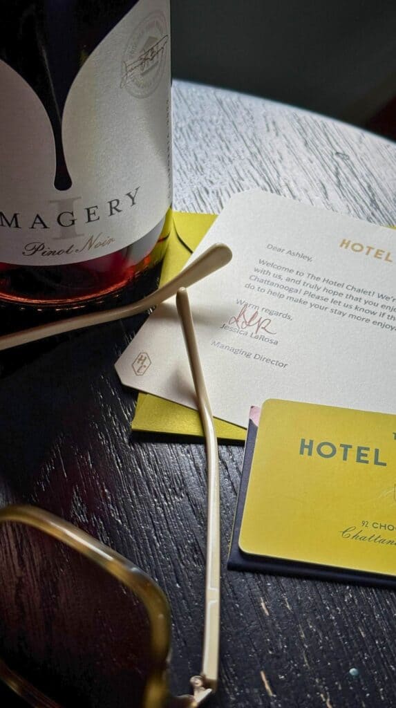 Bottle of wine, hotel key card, and guest welcome materials arranged on a dark wood table inside a Chattanooga Choo Choo train car suite.