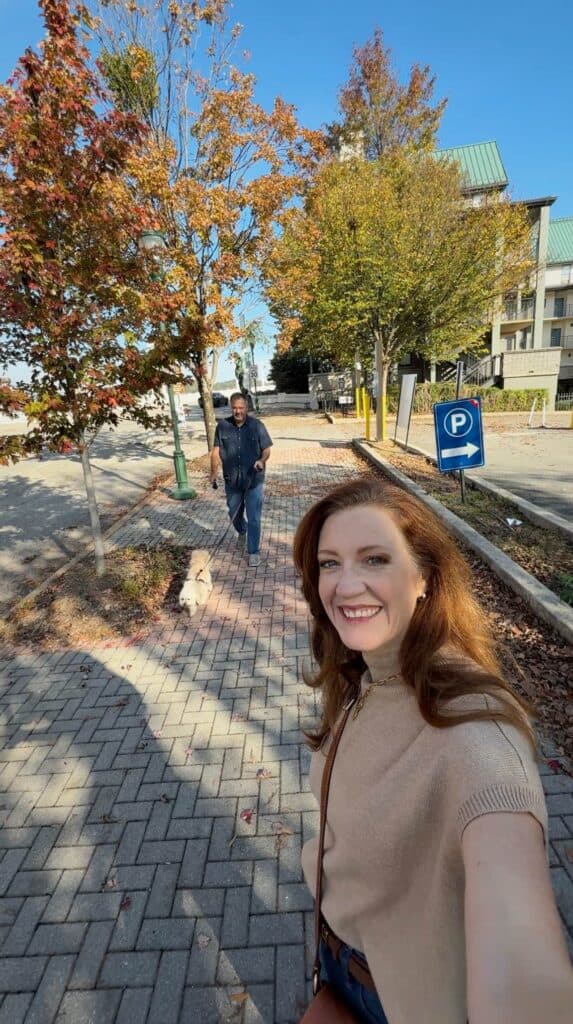 Woman taking a selfie while walking through downtown Chattanooga lined with autumn trees and brick sidewalks during a weekend getaway.