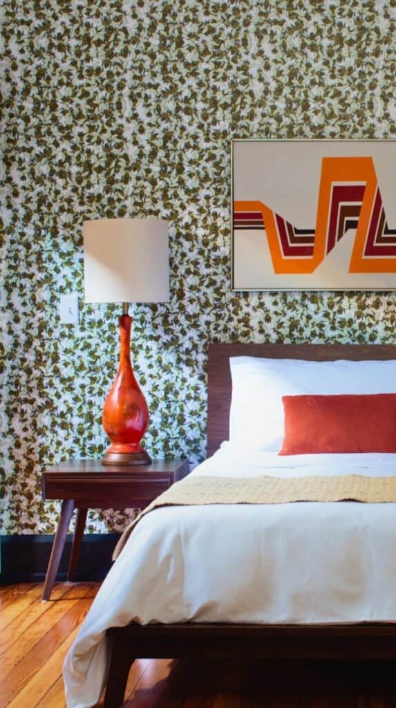 Boutique hotel bedroom at The Dwell Hotel with patterned wallpaper, orange decor accents, and vintage-inspired furnishings.