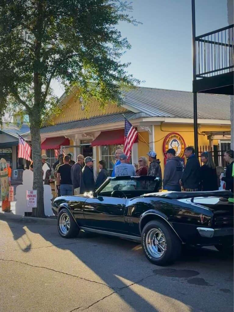 Long line of people outside a small yellow building with an American flag waiting for donuts at a popular Ocean Springs Mississippi restaurant.