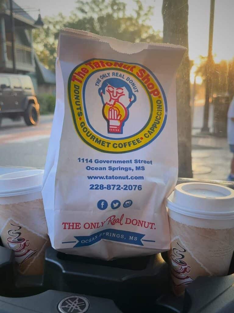 A Tatonut bag and coffees loaded in the golf cart at sunrise, our routine for where to eat in Ocean Springs, MS early.
