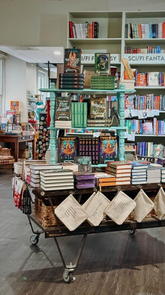 Book tables and genre shelves inside M. Judson Booksellers with stacks of novels, canvas totes, and colorful displays throughout the independent bookstore Greenville visitors should add to their itinerary.