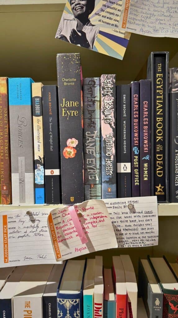 Shelf of classic and contemporary novels with handwritten recommendation cards tucked beneath the books at M. Judson Booksellers.