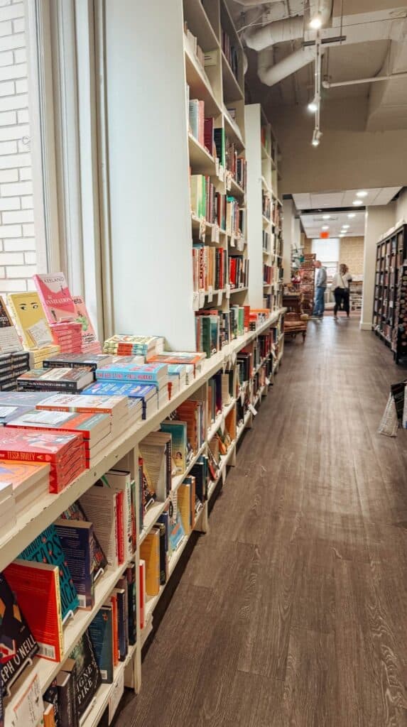 Long aisle lined with bookshelves inside M. Judson Booksellers with natural light streaming through tall windows in the historic Greenville building.