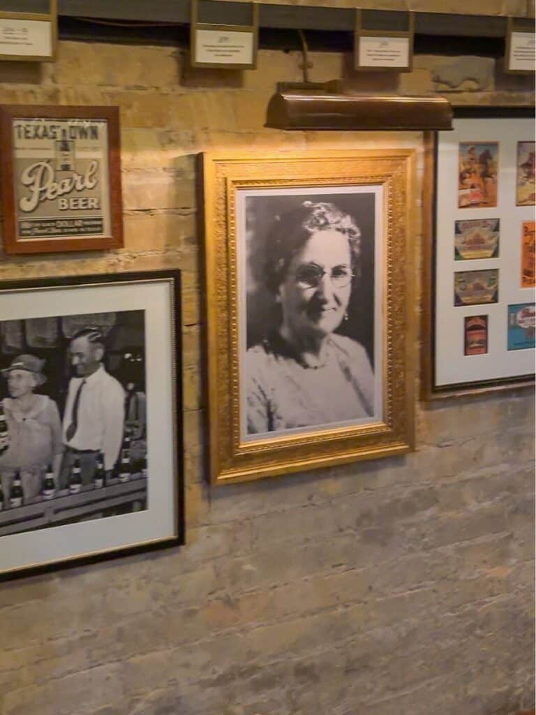Inside Hotel Emma, a framed portrait of Emma hangs beside vintage Pearl Beer photos on the brick wall
