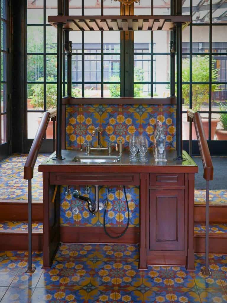 Colorful tiled bar station and copper sink at Hotel Emma San Antonio framed by tall windows