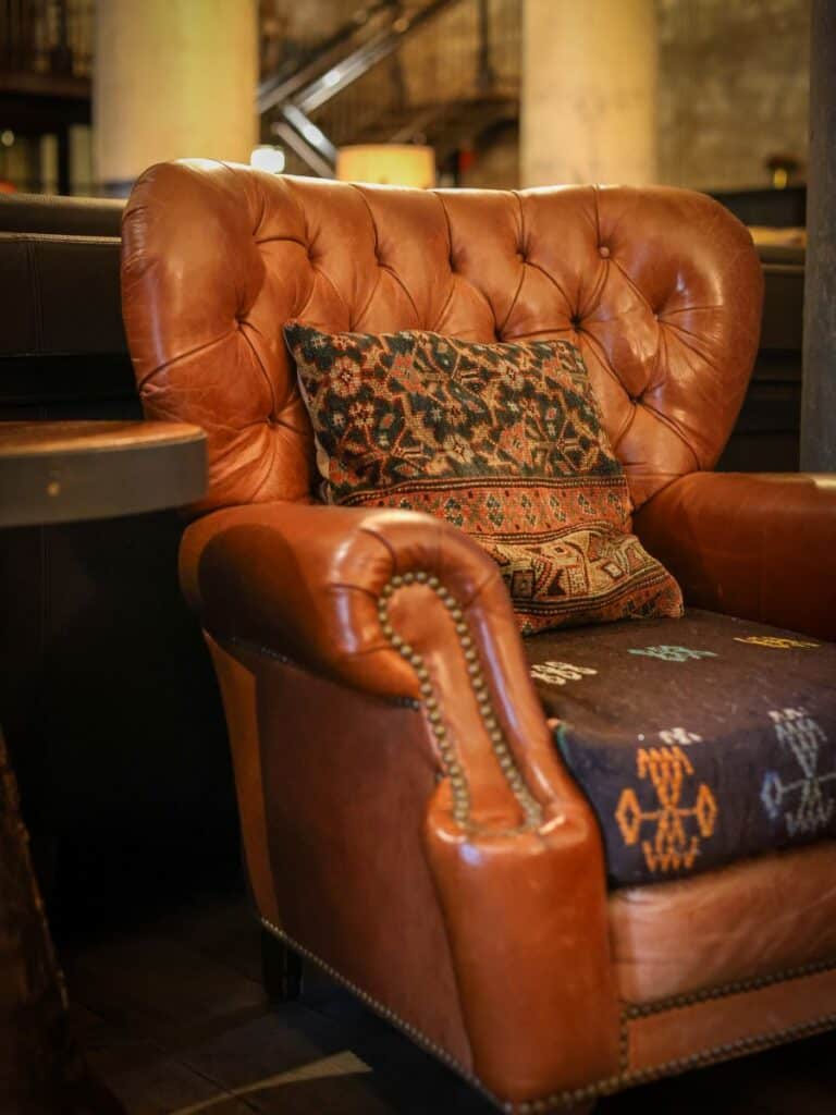 Worn brown tufted leather club chair with a kilim pillow in Hotel Emma San Antonio's Sternewirth