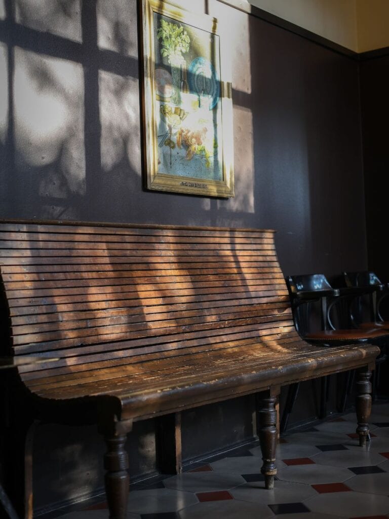 Antique wooden bench at Hotel Emma San Antonio glows in sunlight beneath a framed print