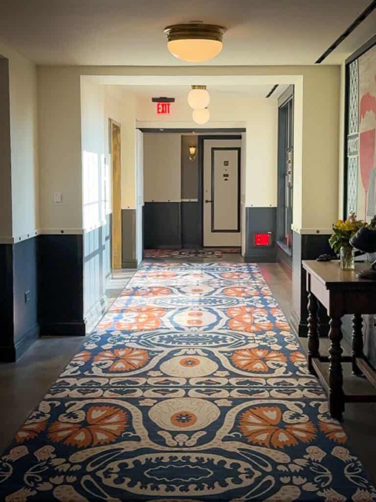 Patterned runner rug leading down a guest hallway at Hotel Emma San Antonio toward the elevators