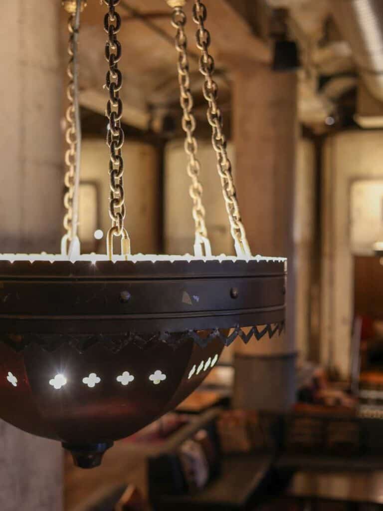 Dark metal chandelier with chains hanging in Hotel Emma, repurposed from original brewery pieces