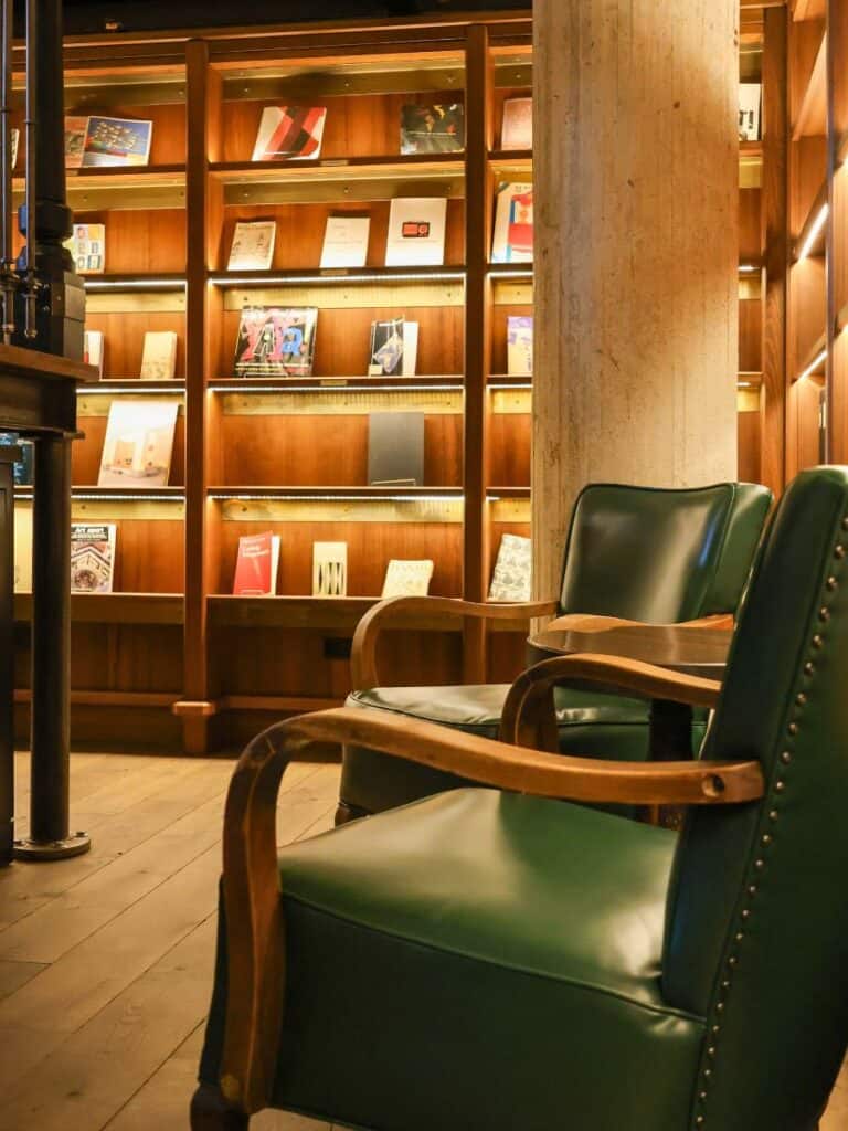 Green leather chairs and lit bookshelves in the Hotel Emma San Antonio Library at night