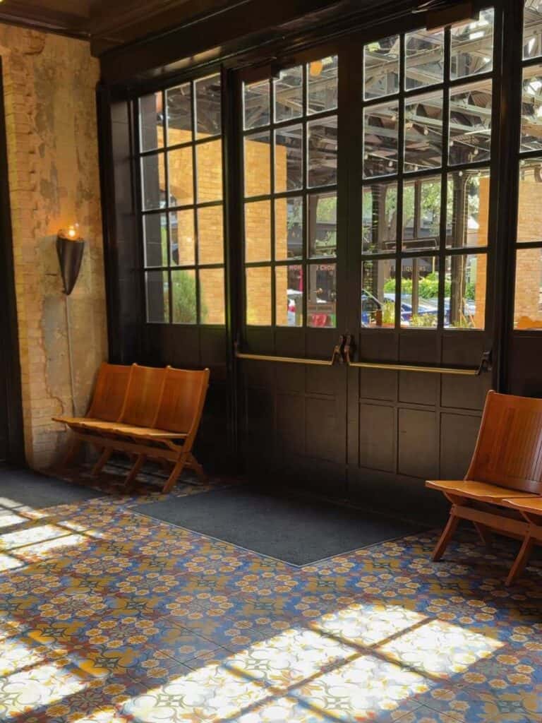 Wooden benches by tall windows at Hotel Emma San Antonio, sunlight falling across patterned tile
