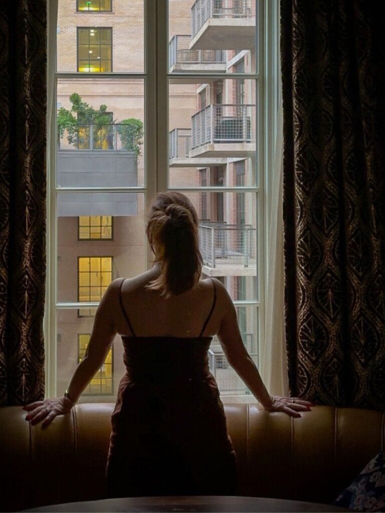 A guest silhouetted against a tall window in her Hotel Emma San Antonio room at dusk