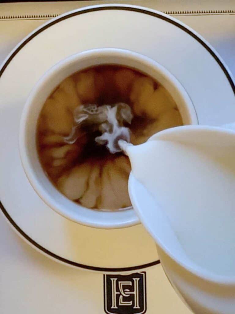 Cream poured into coffee in a cup stamped with the Hotel Emma monogram logo