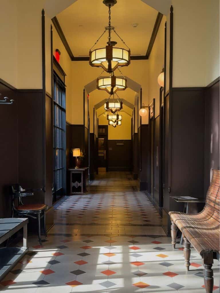 Historic hallway at Hotel Emma San Antonio with tiled floors, dark wainscoting, and hanging chandeliers
