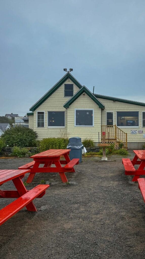 Red picnic tables sit outside a seafood shack
