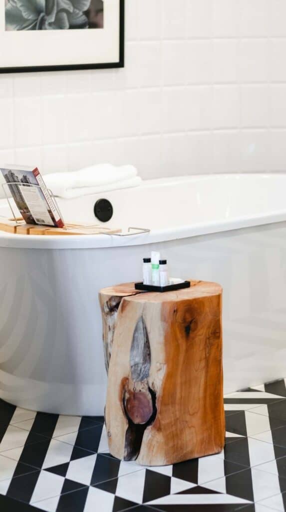 Bathroom with freestanding tub, black and white tile floor, and wood stool in a Vancouver hotel suite.