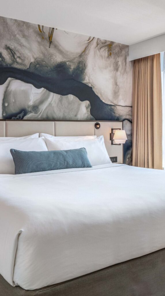 Spacious suite bedroom with white bedding and abstract wall art near Vancouver cruise port.