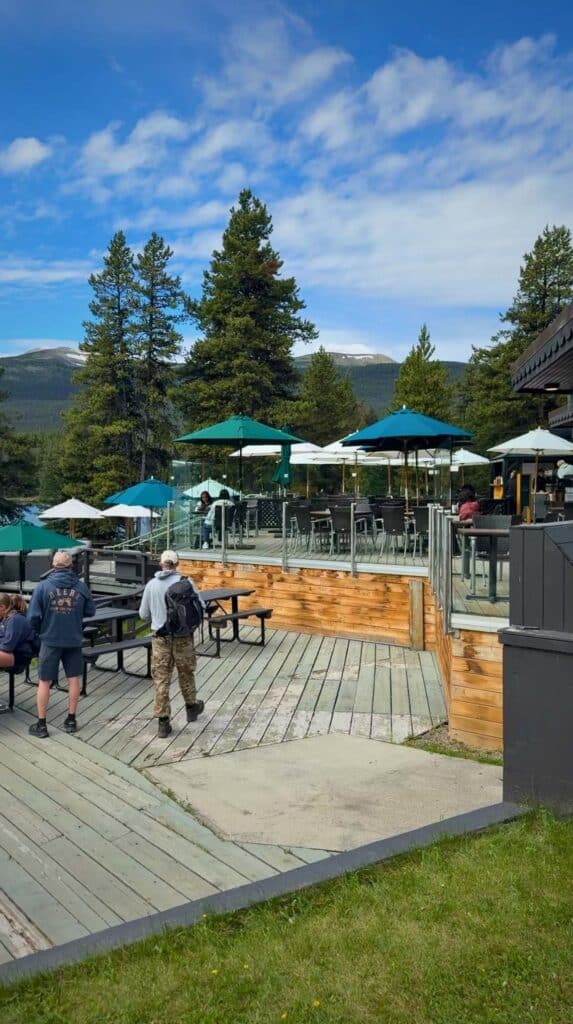 Outdoor patio with tables and umbrellas overlooking Maligne Lake and surrounding mountains.