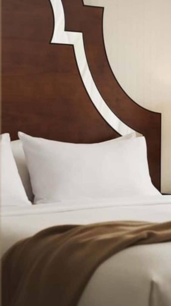 Hotel bed with white linens and wood headboard in a boutique Vancouver hotel room near the cruise port.