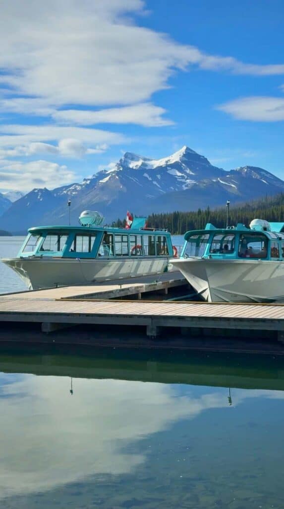 Tour boats docked at Maligne Lake with mountains behind them where visitors begin a boat cruise Maligne Lake.