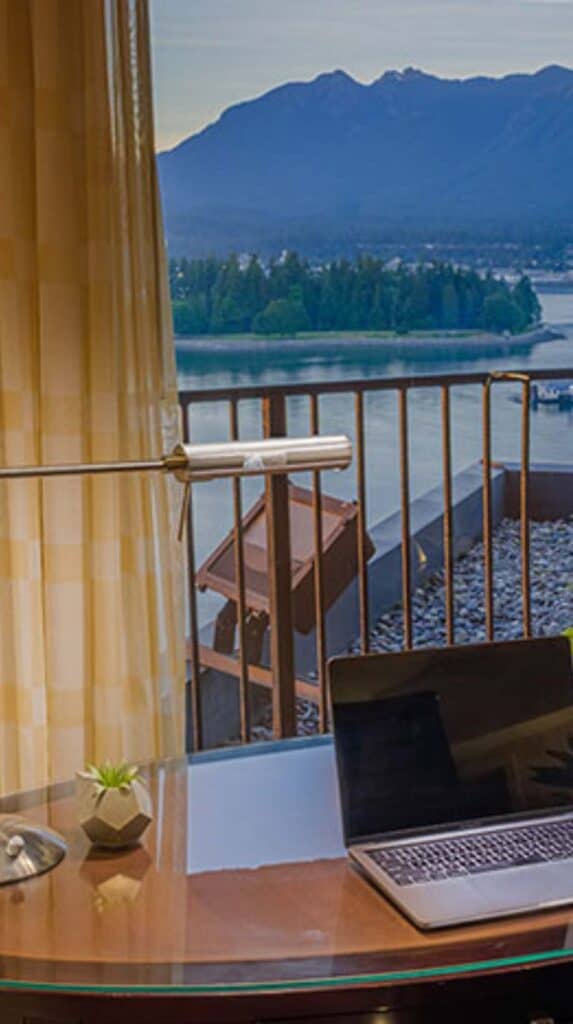 Desk with laptop facing balcony and waterfront view at a Vancouver cruise port hotel.