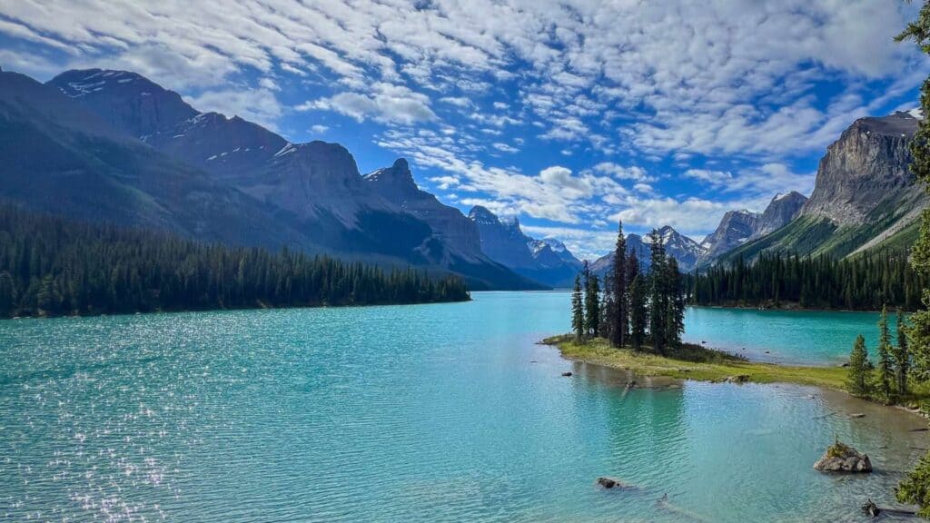 Turquoise Maligne Lake with a small tree covered island and mountain backdrop viewed from a Maligne Lake cruise.