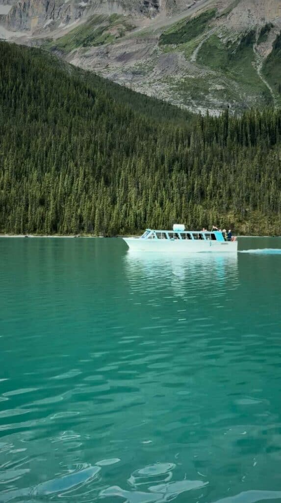 White tour boat moving across turquoise Maligne Lake with forested shoreline and rocky mountains in the background during a boat cruise Maligne Lake.