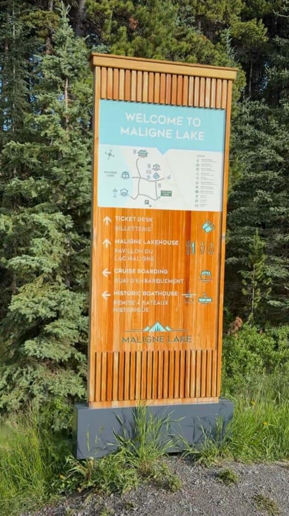 Wooden sign reading "Welcome to Maligne Lake" surrounded by trees at the entrance area.