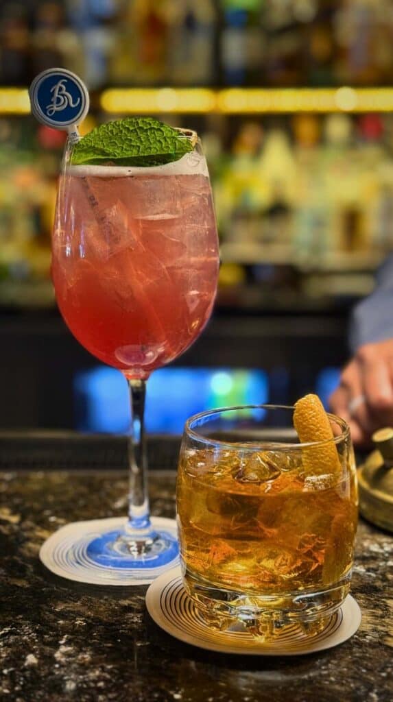 A pink spritz with a Broadmoor pick beside an old fashioned at the Ristorante del Lago bar