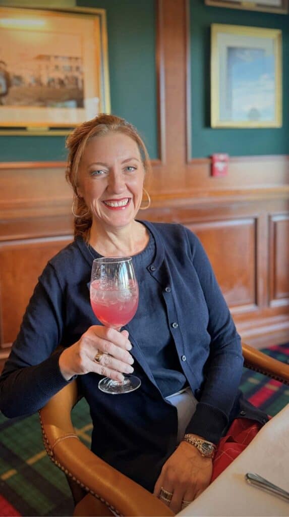 Ashley raising a pink cocktail in the tartan-and-wood dining room at the Grille Broadmoor