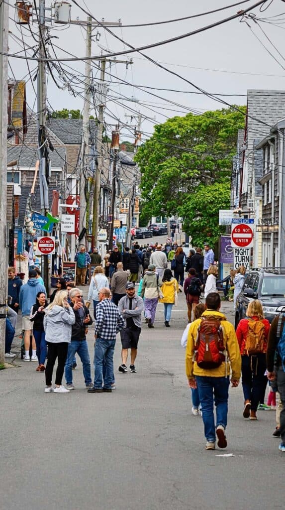 Crowds move through a lively street lined with shops on Cape Ann
